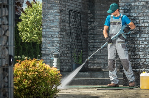 A man in blue shirt using water hose on ground.